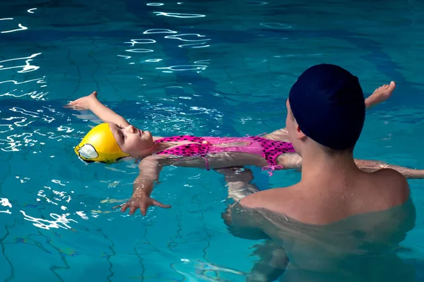 Swimming pool coach teaches a little girl to swim. water activity