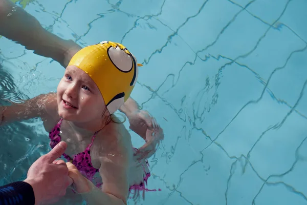 Swimming pool coach teaches a little girl to swim and dive under water, hold breath