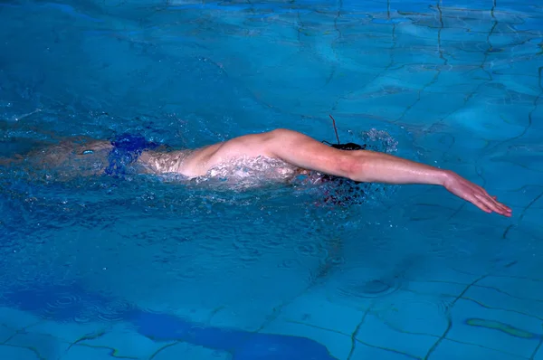 남자는 수영장 실내에서 앞으로 기어가는 스타일로 수영한다 — 스톡 사진