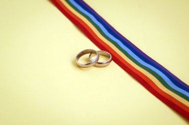 LGBTQ gökkuşağı kurdelesinde sarı arka planda bir çift altın alyans.