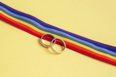 LGBTQ gökkuşağı kurdelesinde sarı arka planda bir çift altın alyans.