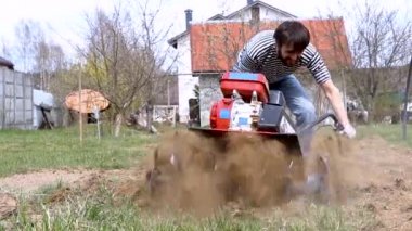 Yaklaş, bahçedeki toprağı ekiciyle süren adam. Tohum ekmek için tarlayı sürme üzerine tarım çalışmaları. Bir adam araziyi motorlu ekicinin yardımıyla sürüyor..