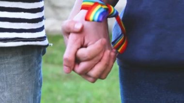 Bileklerinde gökkuşağı LGBT kurdeleleri olan eller. Eşcinsel çift nazikçe el ele tutuşup birbirlerini okşuyor.