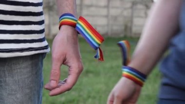 Bileklerinde gökkuşağı LGBT kurdeleleri olan eller. Eşcinsel çift nazikçe el ele tutuşup birbirlerini okşuyor.
