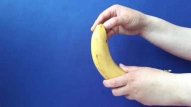 Kadın elleri mavi arka planda bir muzun derisini soyuyor.