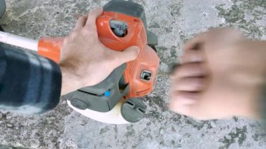 Bahçıvan çim biçme makinesini çalıştırıyor. Eller kolu çeker.