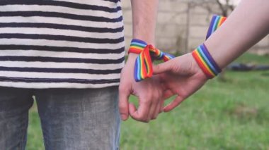 Bileklerinde gökkuşağı LGBT kurdeleleri olan eller. Eşcinsel çift nazikçe el ele tutuşup birbirlerini okşuyor.
