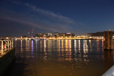 Hollanda 'nın başkenti Amsterdam' ın kanal suları üzerinde romantik bir sonbahar akşamı manzarası. Binaların ve gökdelenlerin ışıkları ve aydınlatmaları arasında.