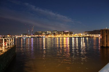 Hollanda 'nın başkenti Amsterdam' ın kanal suları üzerinde romantik bir sonbahar akşamı manzarası. Binaların ve gökdelenlerin ışıkları ve aydınlatmaları arasında.