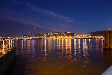 Hollanda 'nın başkenti Amsterdam' ın kanal suları üzerinde romantik bir sonbahar akşamı manzarası. Binaların ve gökdelenlerin ışıkları ve aydınlatmaları arasında.