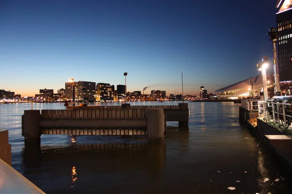 Hollanda 'nın başkenti Amsterdam' ın kanal suları üzerinde romantik bir sonbahar akşamı manzarası. Binaların ve gökdelenlerin ışıkları ve aydınlatmaları arasında. — Stok fotoğraf