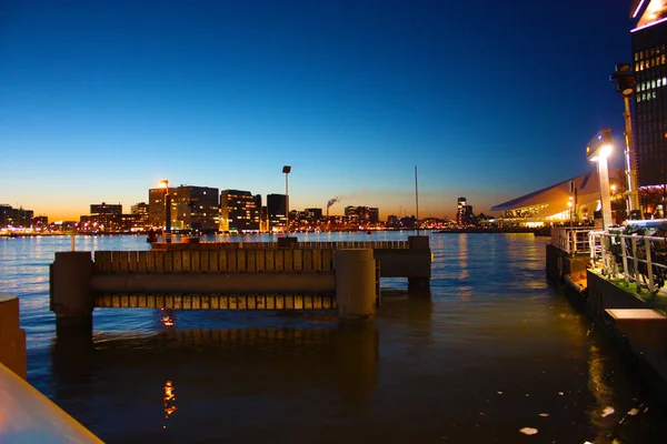 建物や高層ビルの照明や照明の中で、アムステルダムのオランダの大都市の運河の水の上にロマンチックな秋の夜のパノラマ — ストック写真