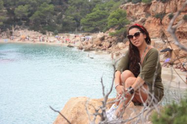 Yazlık kıyafetleriyle mutlu Avrupalı kız Eylül 'de İbiza' da tatilde. Cala Salada 'da, Balear Denizi' nin üzerindeki bir uçurumda oturuyor.
