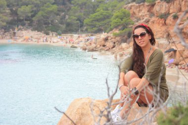 Yazlık kıyafetleriyle mutlu Avrupalı kız Eylül 'de İbiza' da tatilde. Cala Salada 'da, Balear Denizi' nin üzerindeki bir uçurumda oturuyor.