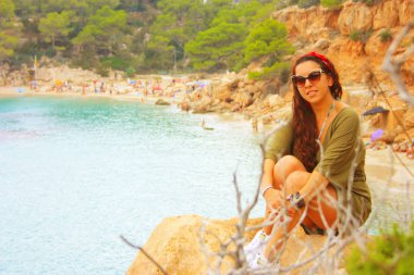 Yazlık kıyafetleriyle mutlu Avrupalı kız Eylül 'de İbiza' da tatilde. Cala Salada 'da, Balear Denizi' nin üzerindeki bir uçurumda oturuyor.