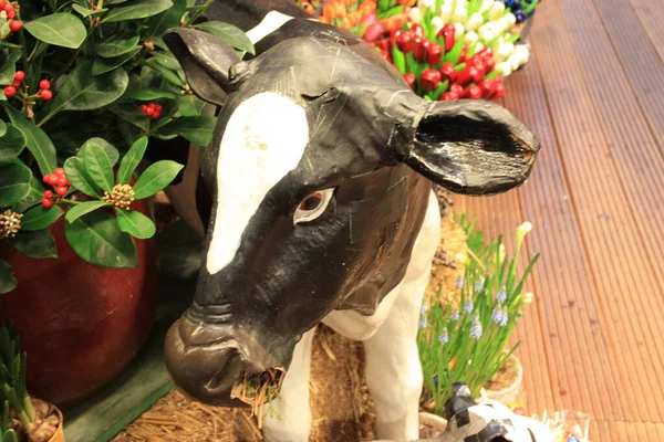 Белая корова с черными пятнами и фальшивым пластиком, которая пасет сено среди букетов фальшивых цветов в сувенирном магазине — стоковое фото