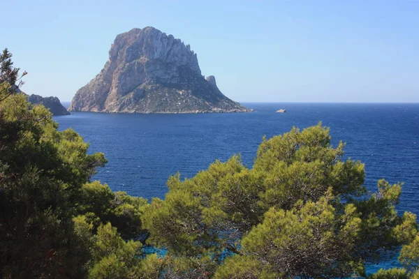 A ilhota solitária de es Vedra em contraste com o mar azul de Ibiza imerso na natureza selvagem verde e árida — Fotografia de Stock