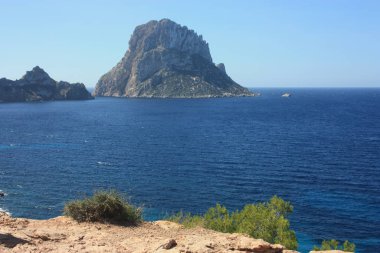 Es Vedra adası. Mavi gökyüzü ve mavi deniz arasında. Balear Adaları 'ndaki Cala D' Hort sahilinin önündeki İbizan kıyıları.