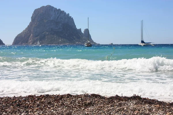 The island of Es Vedra between the blue sky and the blue sea of ​​the Ibizan coasts in front of the Cala D'Hort beach in the Balearic Islands — стокове фото