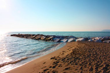 Sahilin önündeki deniz suyunda gün batımında kayalar sıralanır versilia ve parlak renklerle.