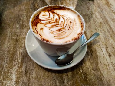 Ahşap masa ve beyaz fincan İtalyan kapuçinosu kremalı ve kakaolu çikolata bir barda yaprak çizer.