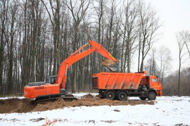 Kış boyunca inşaat alanında kazıcı ve çöp kamyonu.