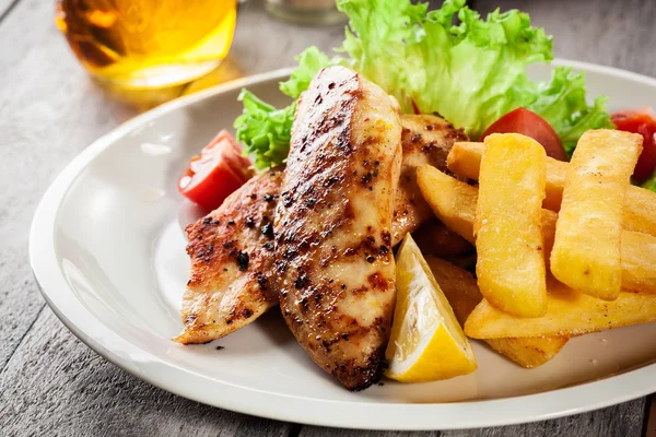 Grilled chicken breasts served with fries and fresh salad — Stock Photo, Image