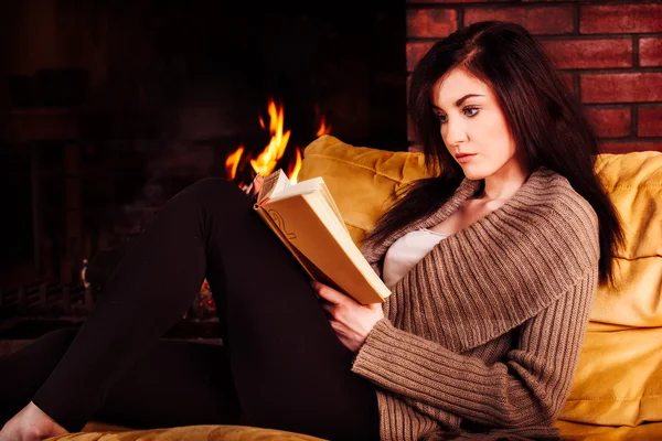 Jovem mulher lendo um livro por lareira — Fotografia de Stock