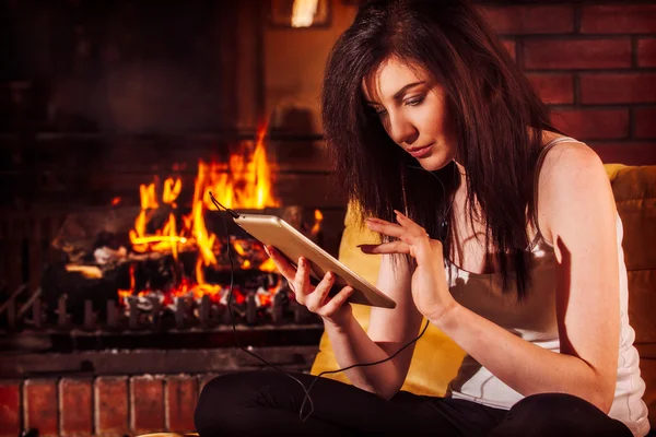 Mujer usando tableta digital sentada junto a la chimenea —  Fotos de Stock