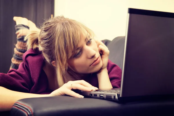 Ung kvinna med blont hår arbetar på hennes laptop hemma — Stockfoto