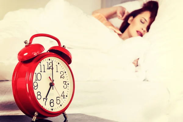 Sleeping woman with her hand touching alarm clock on bed — Stock Photo, Image