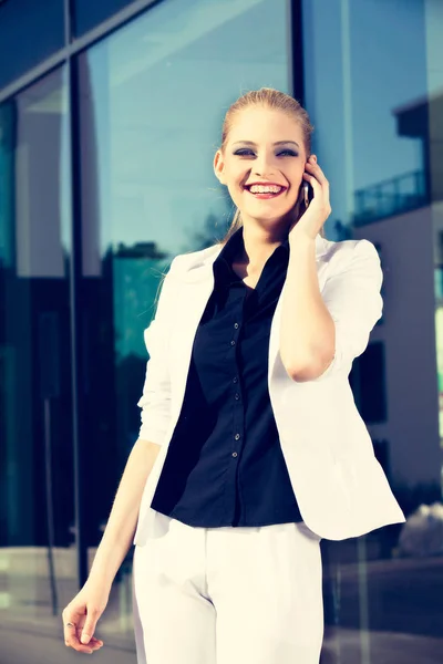 Young business woman talking a mobile phone on street against building — Stock Photo, Image