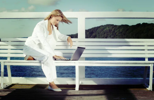 在闲暇时间工作。年轻的金发女子，在码头上的笔记本电脑 — 图库照片