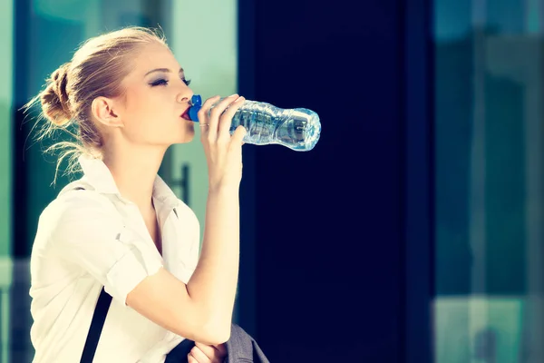 Молодая деловая женщина пьет воду из маленькой бутылочки — стоковое фото