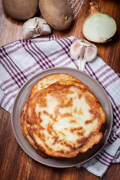 Stack of potato pancakes on a wooden table. In the background po — Stock Photo, Image