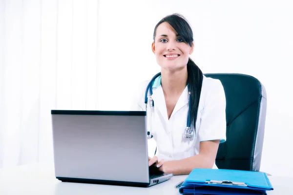 Medico femminile seduto alla scrivania dell'ufficio e sorridente alla fotocamera — Foto Stock