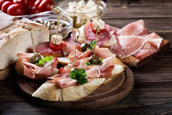 Tapas españolas con rebanadas de jamón serrano, salami, aceitunas y cubos de queso en una mesa de madera — Foto de Stock