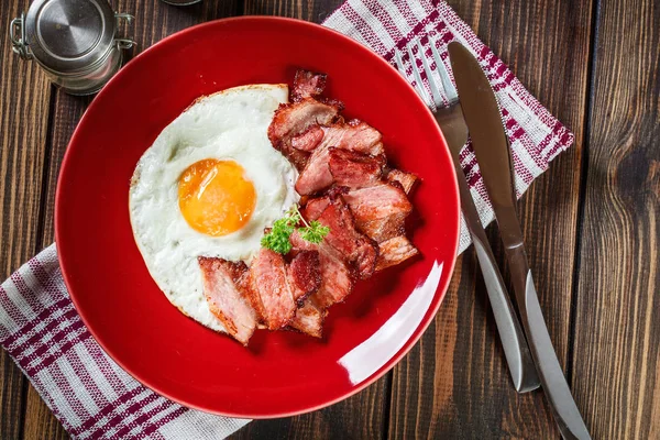 Fatias de bacon defumado e ovo frito em uma placa vermelha — Fotografia de Stock