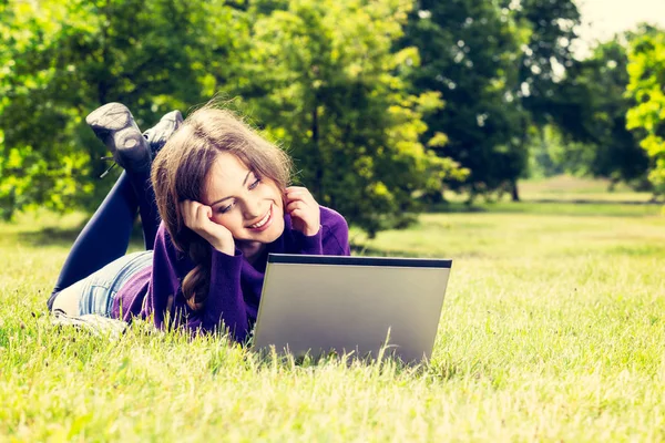 Młoda kobieta korzysta z laptopa w parku, leżącego na zielonej trawie — Zdjęcie stockowe