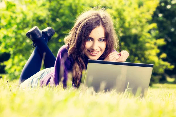 若い女性の緑の草の上に横たわる公園でラップトップを使用して — ストック写真