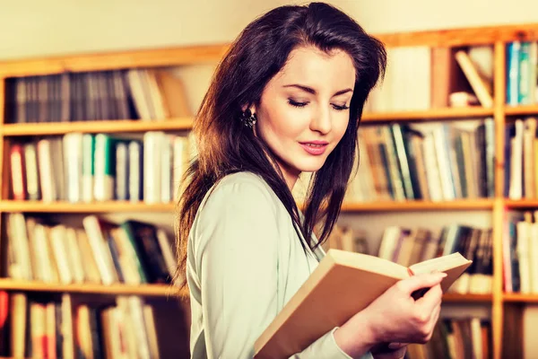 Jovem mulher lendo um livro na frente de estantes — Fotografia de Stock