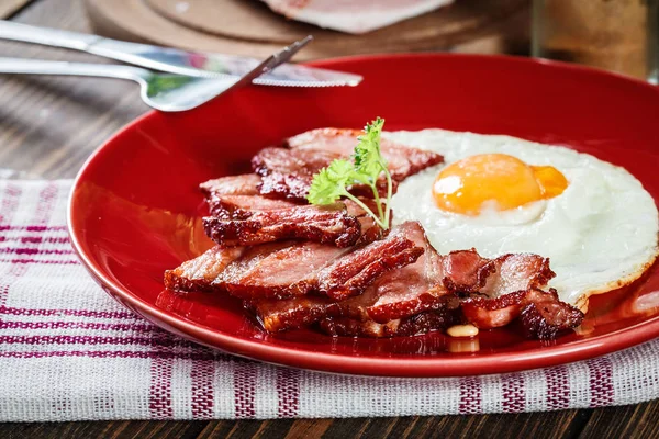 Rebanadas de tocino ahumado y huevo frito en un plato rojo —  Fotos de Stock