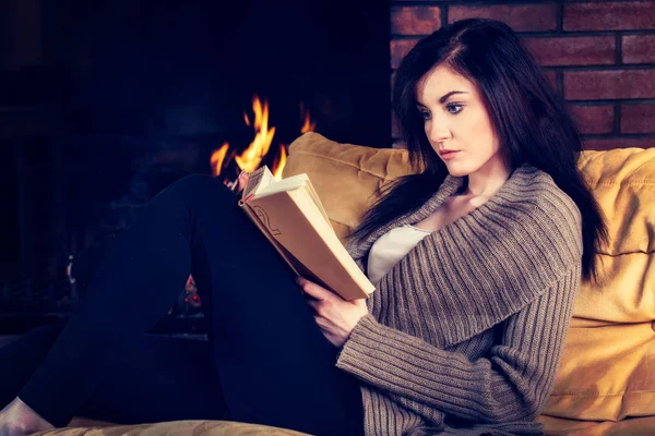 Junge Frau liest ein Buch am Kamin — Stockfoto