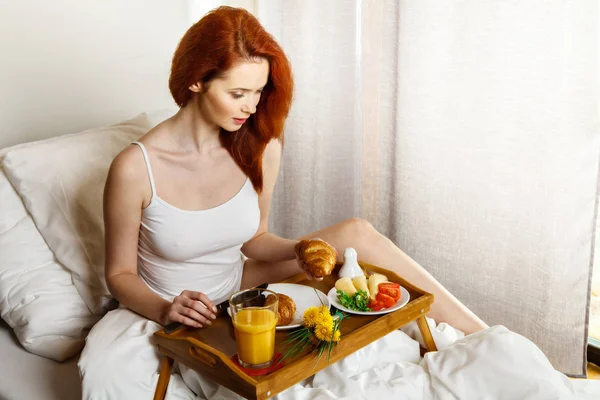 若い女性は、朝はベッドで朝食を食べる — ストック写真