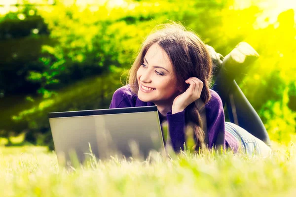 Jonge vrouw met laptop in het park liggen op het groene gras — Stockfoto