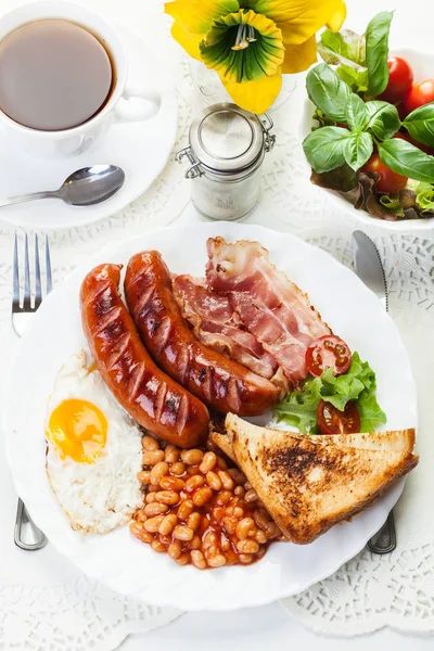 Полный английский завтрак с беконом, колбасой, жареным яйцом и выпечкой — стоковое фото