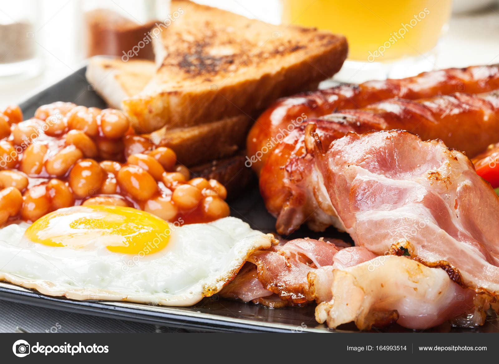 Full English breakfast with bacon, sausage, egg, baked beans and orange juice Stock Photo by