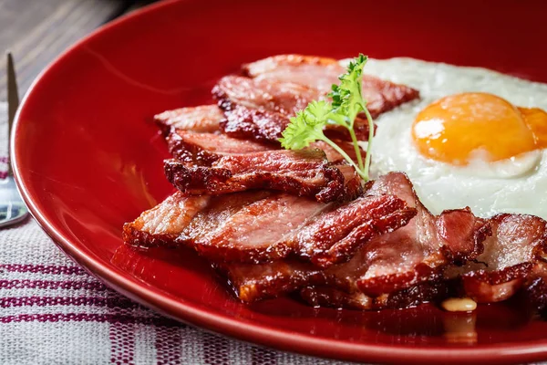 Fette di pancetta affumicata e uovo fritto su un piatto rosso — Foto Stock
