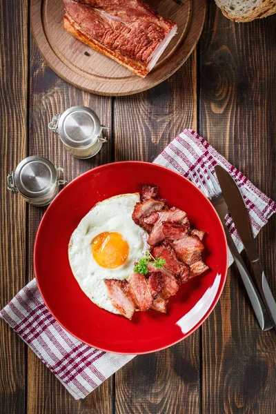 Sneetjes gerookte bacon en gebakken ei op een rode plaat — Stockfoto