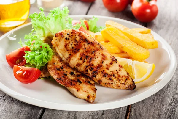 Grilled chicken breasts served with fries and fresh salad — Stock Photo, Image